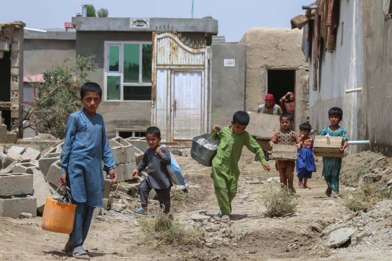 Anak-anak Afghanistan membawa barang-barang mereka setelah banjir bandang di daerah Khair Abad provinsi Ghazni
