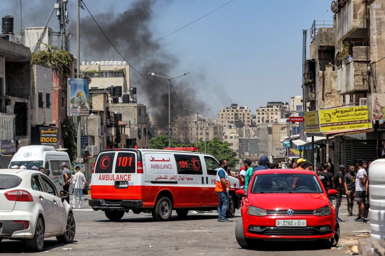 People gather near a Palestinian Red Crescent ambulance as smoke rises in the air from burning tires further ahead along a road at al-Ain camp for Palestinian refugees, west of Nablus in the occupied West Bank, on July 26, 2023 during an Israeli army raid. (Photo by Zain JAAFAR / AFP)