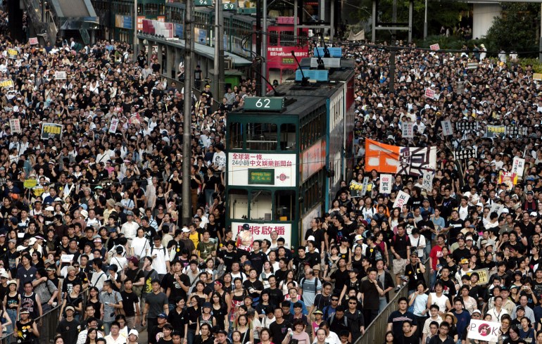 Massaal protest in Hong Kong in 2003 over een geplande veiligheidswet.  Er staat een dubbeldekkerbus in de menigte