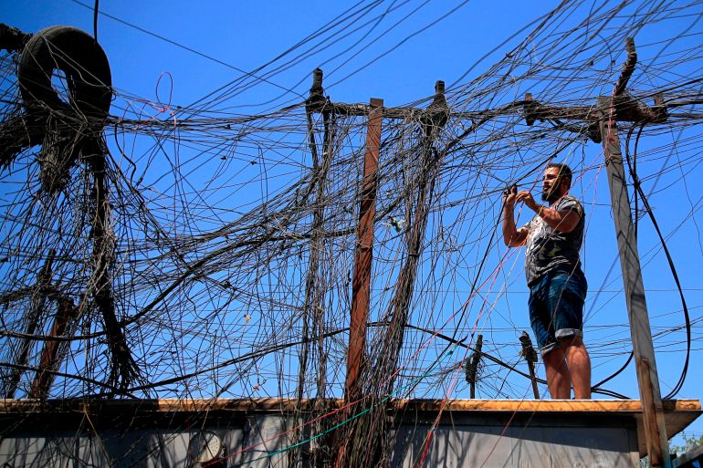 Man on a rooftop trying to connect a huge tangle of electric wires