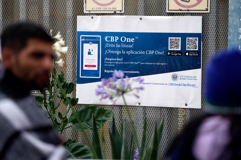 A sign advertises the CBP One mobile app as asylum seekers pass by.