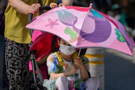 A child sits on a stroller holding an umbrella to shield from the sun as the capital city was hit by heatwave in Beijing, Monday, June 5, 2023. (AP Photo/Andy Wong)