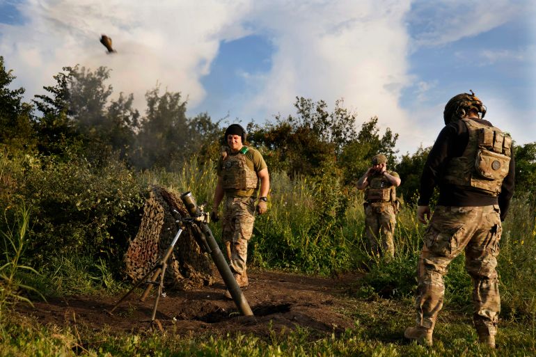 Üç Ukraynalı asker, Bakhmut yakınlarındaki cephe hattında Ruslara havan topları atıyor.  Harcın havaya yükseldiği görülebilir.