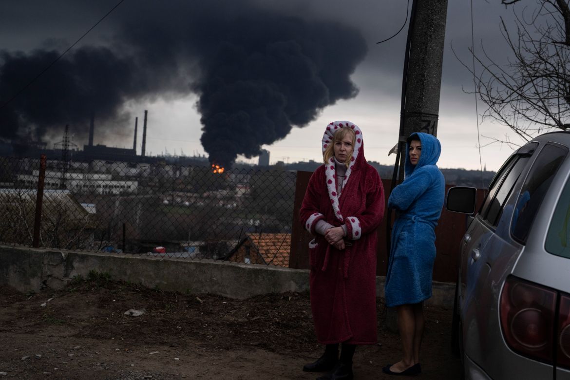 Women stand next to a car as smoke rises in the air in the background after shelling in Odesa,