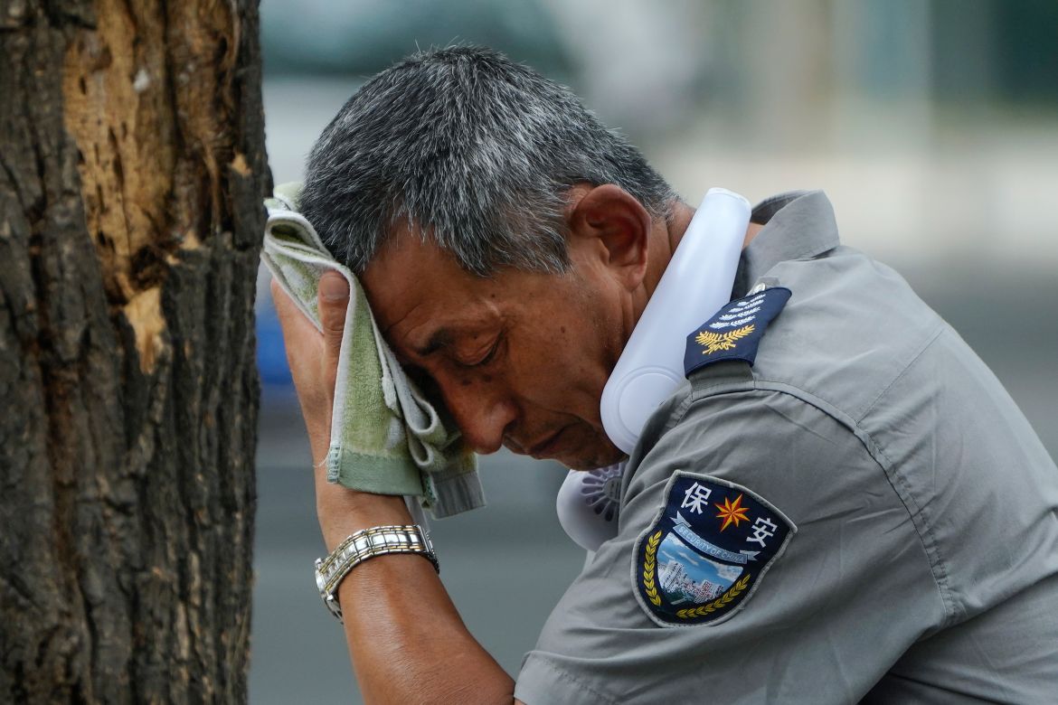 A security guard wearing an electric fan on his neck wipes his sweat on a hot day in Beijing,