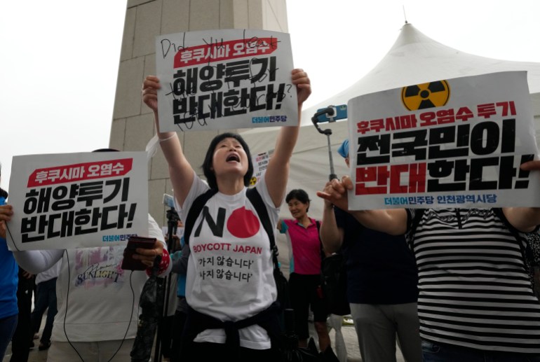 Manifestantes em uma manifestação contra o plano de liberação de água de Fukushima na Coreia do Sul.  Eles estão segurando cartazes escritos em coreano.  A mulher na frente está vestindo uma camiseta onde se lê 'NÃO' e embaixo 'Boicote o Japão'