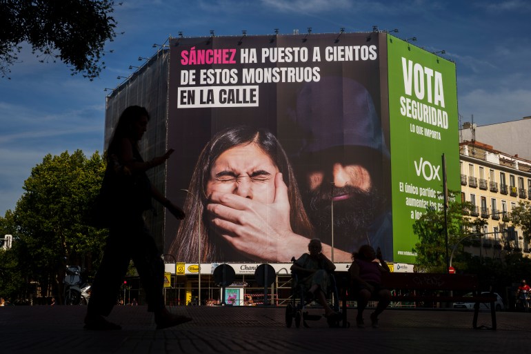 Une femme passe devant une affiche électorale géante du parti d'extrême droite VOX lisant en espagnol : "Sanchez a mis des centaines de ces monstres dans la rue.  Votez en toute sécurité.  Ce qui importe" suspendu à un immeuble de Madrid,