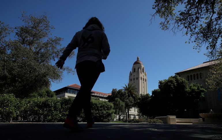 A figure, in shadow, walks across the Stanford campus.  The Hoover Tower can be seen in front of them.