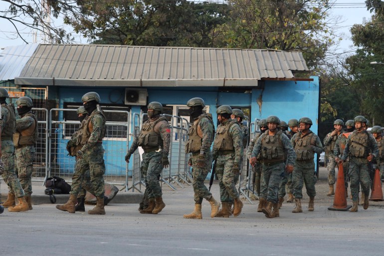 A line of soldiers stand in front of a one-story blue building.