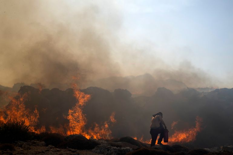 A man tries to extinguish a fire, near the seaside resort of Lindos, on the Aegean Sea island of Rhodes, southeastern Greece, on Monday, July 24, 2023.