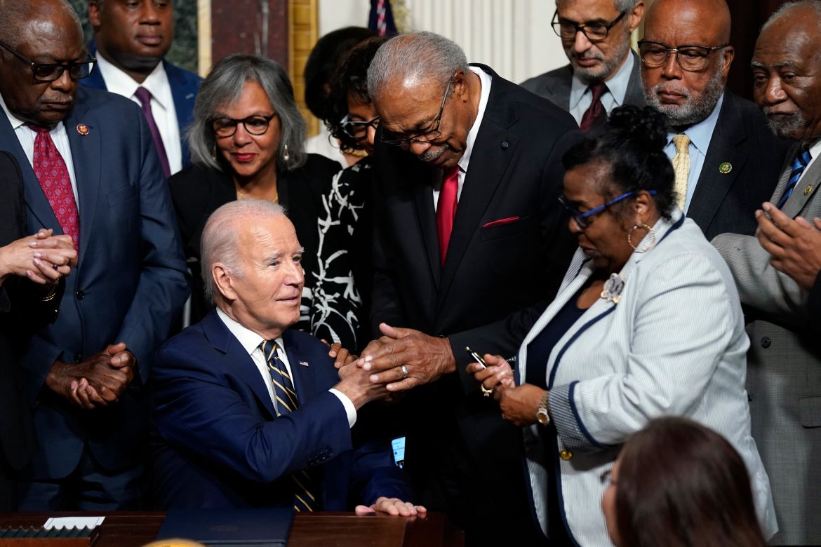 President Joe Biden shakes hands with Rev. Wheeler Parker as Marvel Parker holds a signing pen