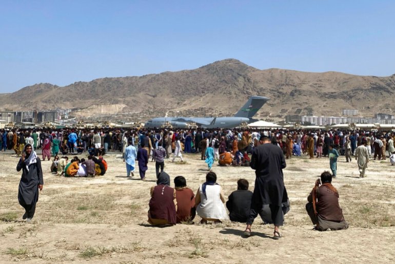 People sit in a field next to an airport during the US withdrawal from Afghanistan