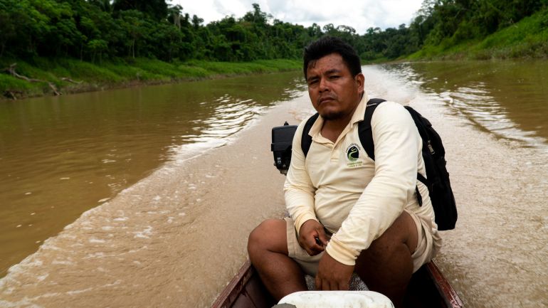 A man in a yellow polo shirt and backpack guides a canoe along an Amazon river.