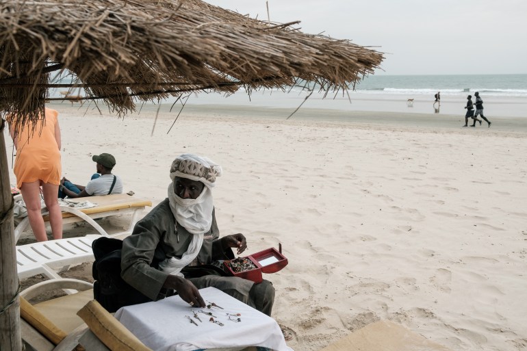 Almounzer Dicko menyiapkan meja pajangan dan mengambil perhiasan dari kotak dan tas yang dia bawa di sekitar Cap Skirring di Casamance saat dia membawa perhiasannya di tas dan kotak dari Mali yang mendekati turis di pantai untuk membeli produknya