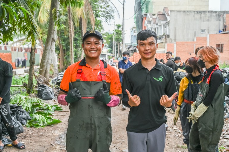 Two volunteers smiile and give the thumbs up. One is wearing green ribber waders