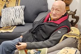 Tsultrim pictured in New York, He is seated ona grey sofa and wearing a fleece-style jacket with a body warmer. He is bald.