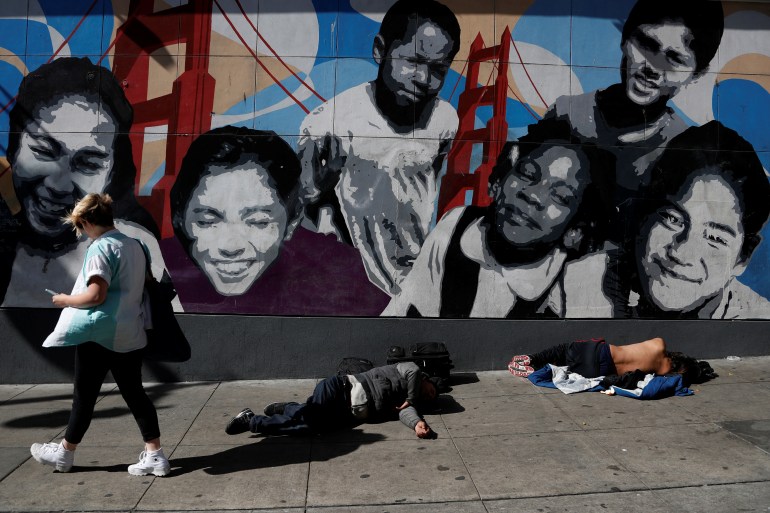 A woman walks past men passed out on the sidewalk n the Tenderloin area of San Francisco, California, US