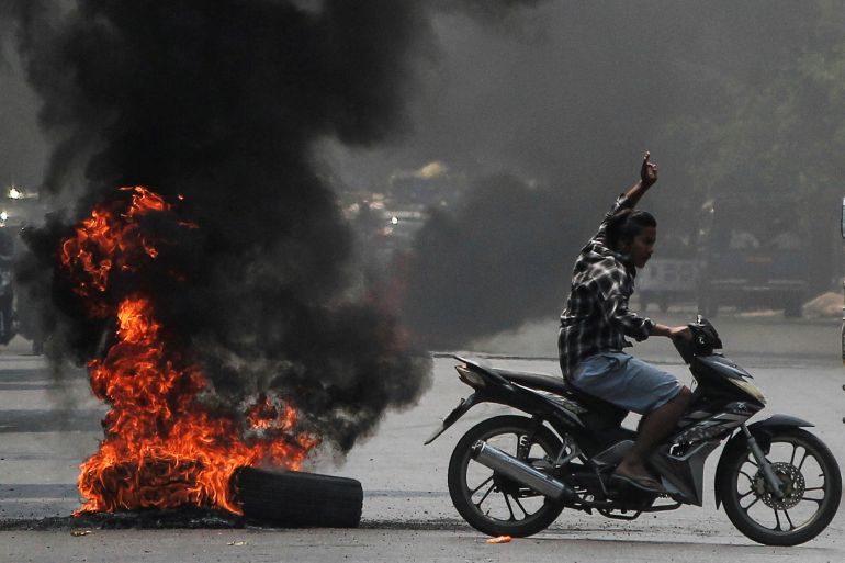 A man flashes the three-finger salute as he passes burning tires during a protest against the military coup, in Mandalay, Myanmar April 1, 2021.
