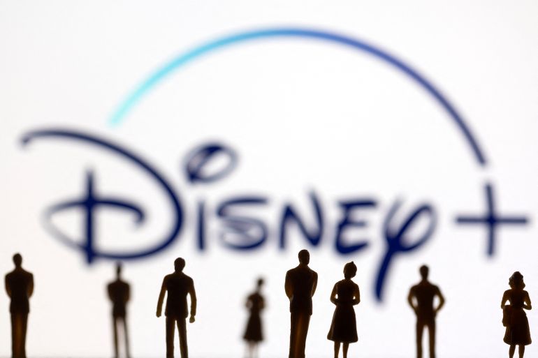 Toy figures of people are seen in front of the displayed Disney +