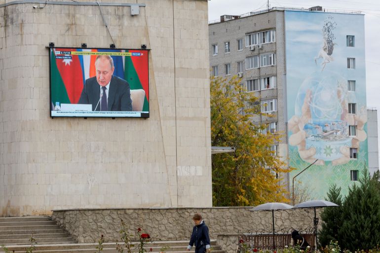 Russia's President Vladimir Putin is seen on a screen during the broadcast of a Russian state TV news report as a local resident walks near an apartment block decorated with a mural, an element of which depicts a nuclear power plant, in the course of Russia-Ukraine conflict in the city of Enerhodar in the Zaporizhzhia region, Russian-controlled Ukraine, October 14, 2022. REUTERS/Alexander Ermochenko