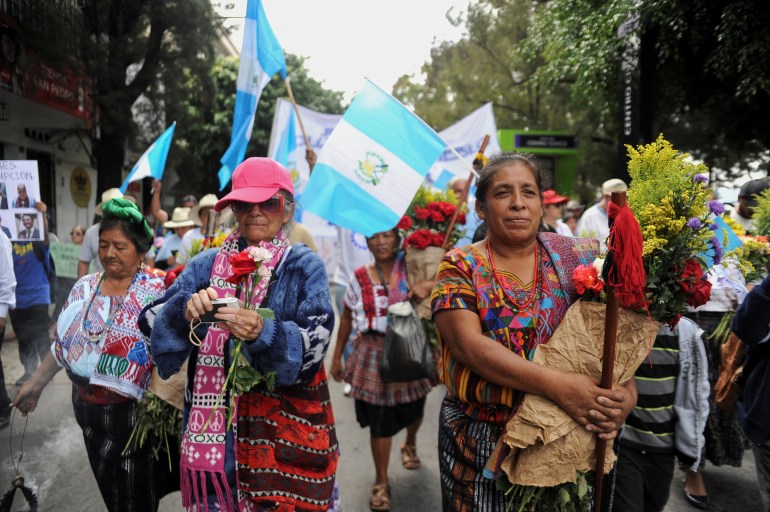 People march with bouquets of flowers and Guatemalan flags through the streets of Guatemala City.