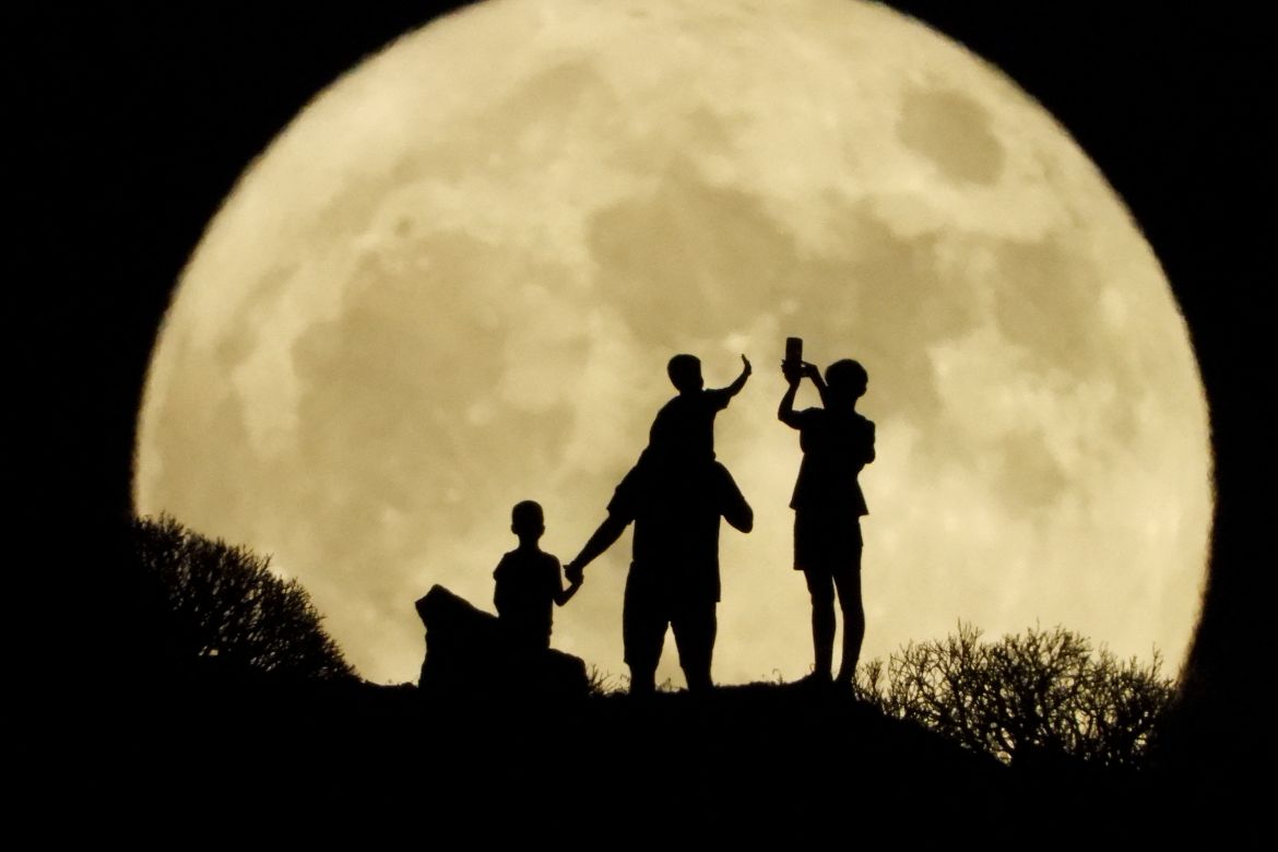 A family stand with the full moon known as the "Sturgeon Moon" in the background, in Arguineguin, in the island of Gran Canaria, Spain