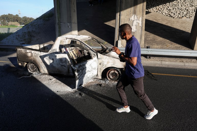 A man runs past a burnt out vehicle which was set alight during a protest by taxi operators over a number of grievances against traffic authorities in Cape Town, South Africa, August 3, 2023. REUTERS/Esa Alexander