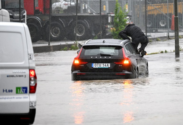 A man climbs out of a car that tried to get through a flooded roundabout in Arlov on the closed flooded E6 outside Malmo, Sweden