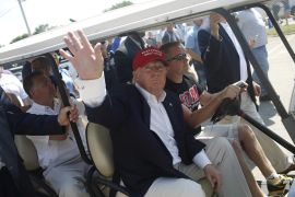 Wearing a "Make America Great Again" baseball camp, Donald Trump waves from inside a golf cart.