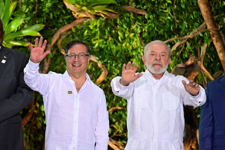 Two men — Gustavo Petro and Luiz Inacio Lula da Silva — wave and raise their arms at photo opportunity during the Amazon summit. Both men wear white shirts.