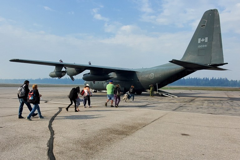 People walk to a Royal Canadian Air Force transport plane while being evacuated from an approaching wildfire in Hay River, Northwest Territories, Canada August 14, 2023. Canadian Forces/Handout via REUTERS THIS IMAGE HAS BEEN SUPPLIED BY A THIRD PARTY.