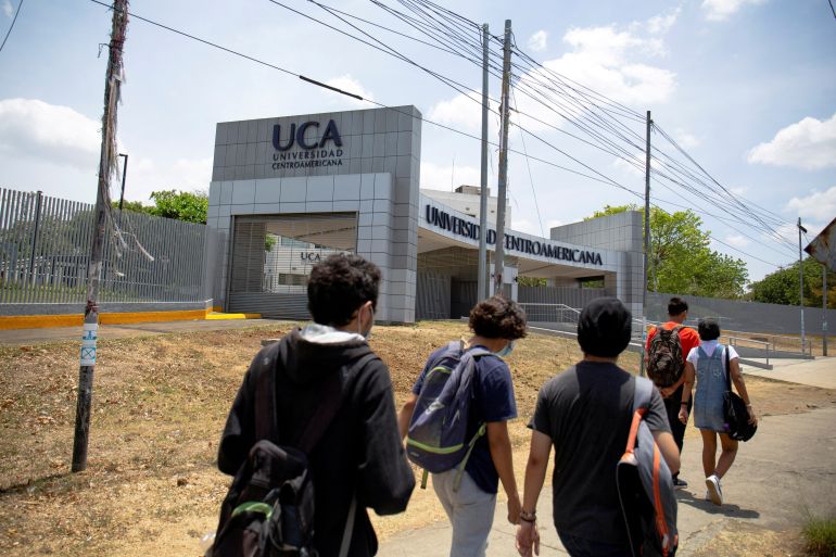 Students walk by the entrance to a school, with the letters "UCA" written about the gateway.