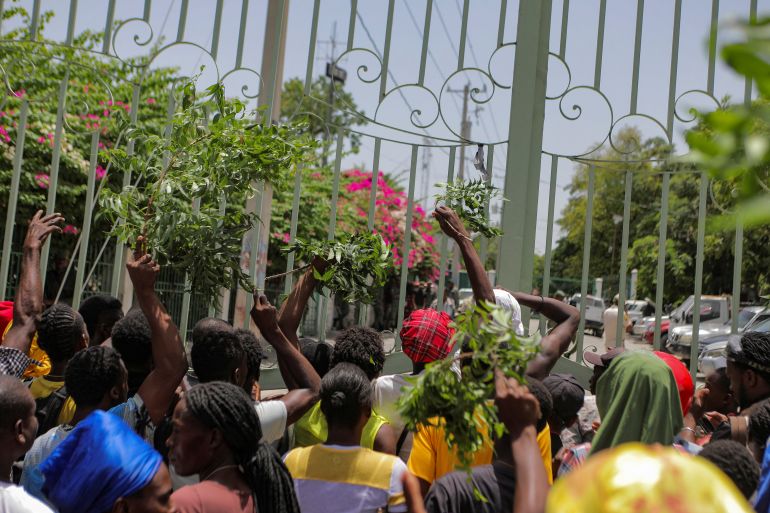 Residents of the neighbourhood Carrefour Feuilles gather outside a military base demanding help after they had to flee their homes when gangs took over, in Port-au-Prince, Haiti August 16, 2023. The crowd can be seen raising their hands in protest outside a metal gate.