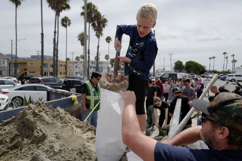 Bradford Slevin and his eight-year-old son, Theo, fill up sandbags to take home as Hurricane Hilary approaches in Long Beach, California
