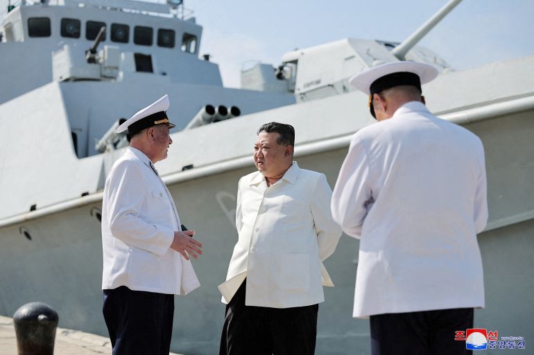Kim Jong Un speaking to naval officers with a ship behind.
