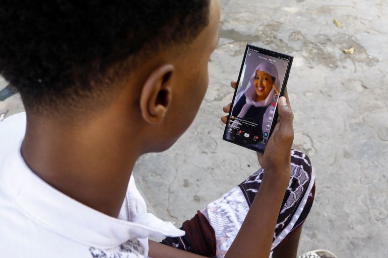 Abdulahi Ahmed uses his mobile phone to watch a video on social media app TikTok, outside his home in Waberi district of Mogadishu, Somalia