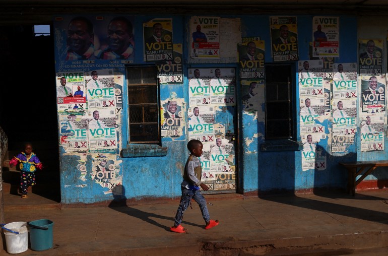 Children walk past election posters ahead of the presidential elections in Mbare township, in Zimbabwe