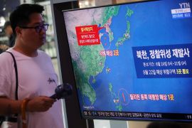 A man in Seoul walking past a large TV screen showing a map of North Korea's satellite launch.