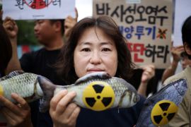 A close up of a woman protesting against the release of the Fukushima water. She is holding a model of a fish with the radiation hazrad symbol on its side