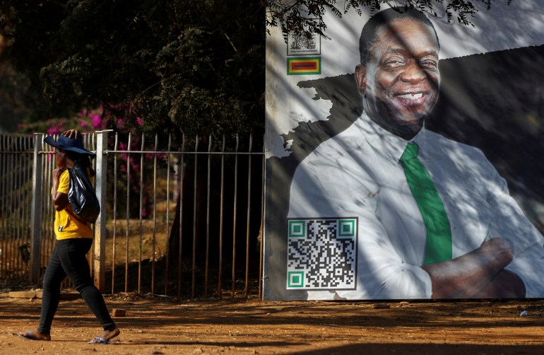 A woman walks by a giant billboard of Zimbabwe's president Emmerson Mnangagwa, with a QR code at the bottom.