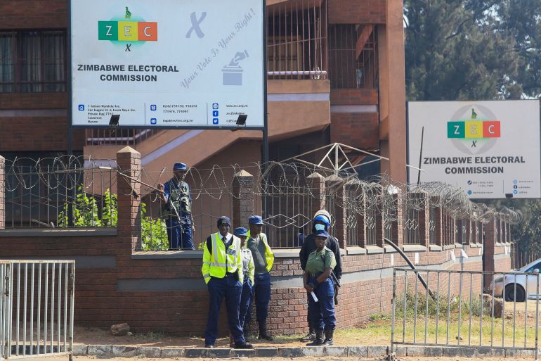 Police stand next to a barricade with razor wire, below a sign indicating the offices of the Zimbabwe Election Commission.