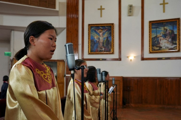 The choir sings during a Sunday mass at Saints Peter and Paul Cathedral in Ulaanbaatar. They are wearing golden gowns and singing into microphones