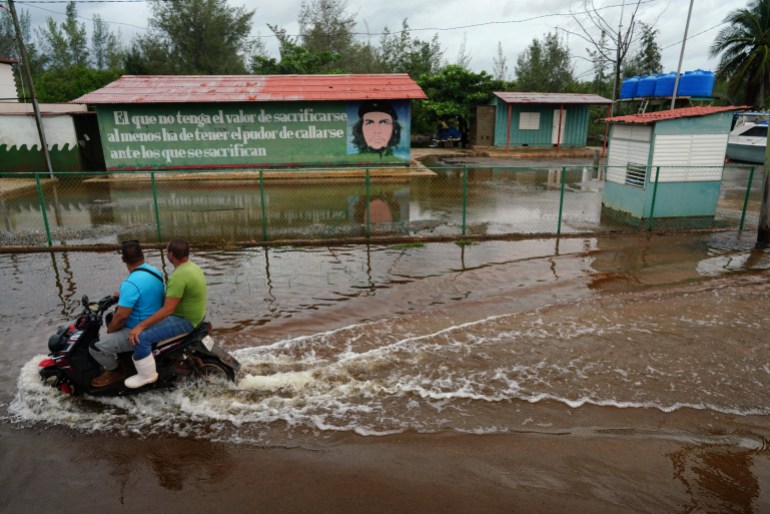 People on a flooded street pass by an image of late revolutionary hero Ernesto "Che" Guevara as Storm Idalia makes landfall in Cuba, in Guanimar, Cuba, August 28, 2023. REUTERS/Alexandre Meneghini