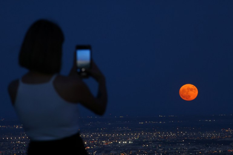 Una donna scatta una foto mentre una super luna, conosciuta come Luna Blu, sorge sopra Ciudad Juarez