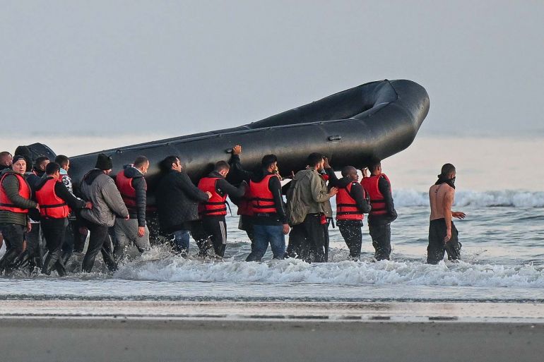 About fourty migrants, fom various origins, hold an inflatable boat before boarding to attempt crossing the Channel illegally to Britain, near the northern French city of Gravelines on July 11, 2022