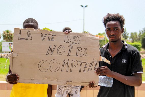 refugees hold up a sign that reads 'Black Lives Matter' in French