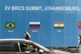 A woman walks past a poster for the 2023 BRICS Summit at the Sandton Convention Centre in Sandton, Johannesburg, on August 20, 2023 [File: Marco Longari/AFP]
