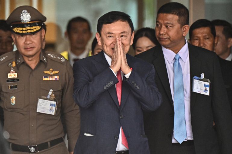 Thaksin Shinawatra smiled and makes a wai gesture on his return to Thailand. A police officer is behind him