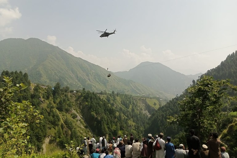 People watch as an army soldier slings down from a helicopter during a rescue mission to recover students stuck in a chairlift in Pashto village of mountainous Khyber Pakhtunkhwa province