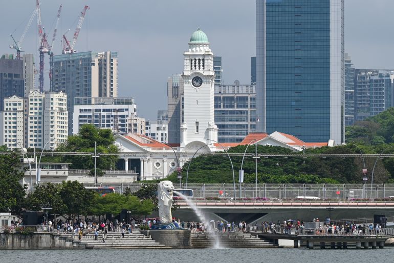 Singapur'un ve ağzından su fışkıran Merlion heykelinin görüntüsü.  İnsanlar oyalanıyor.